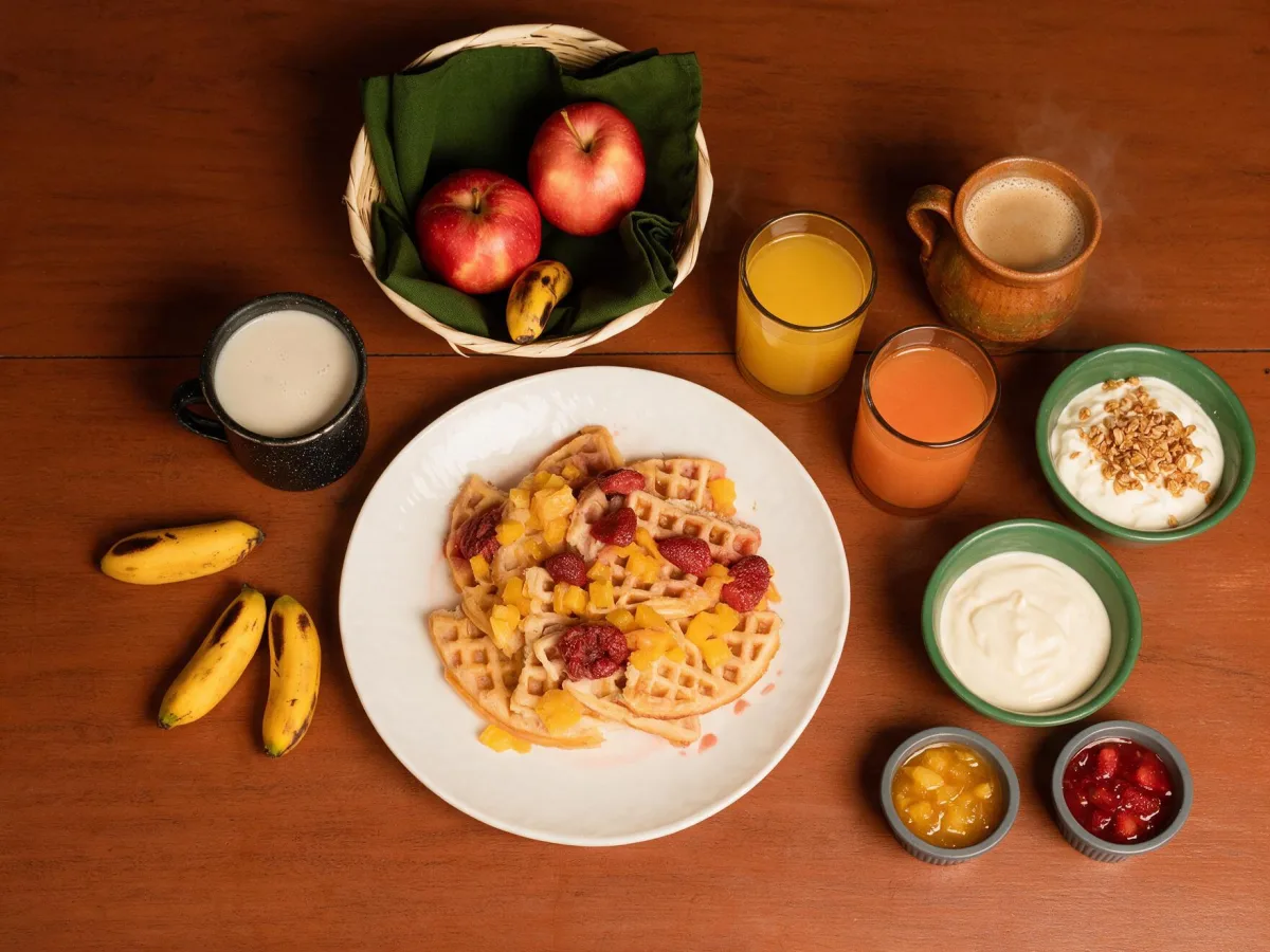 Waffles, fruit, yogurt, granola, coffee and jams arranged on a breakfast table